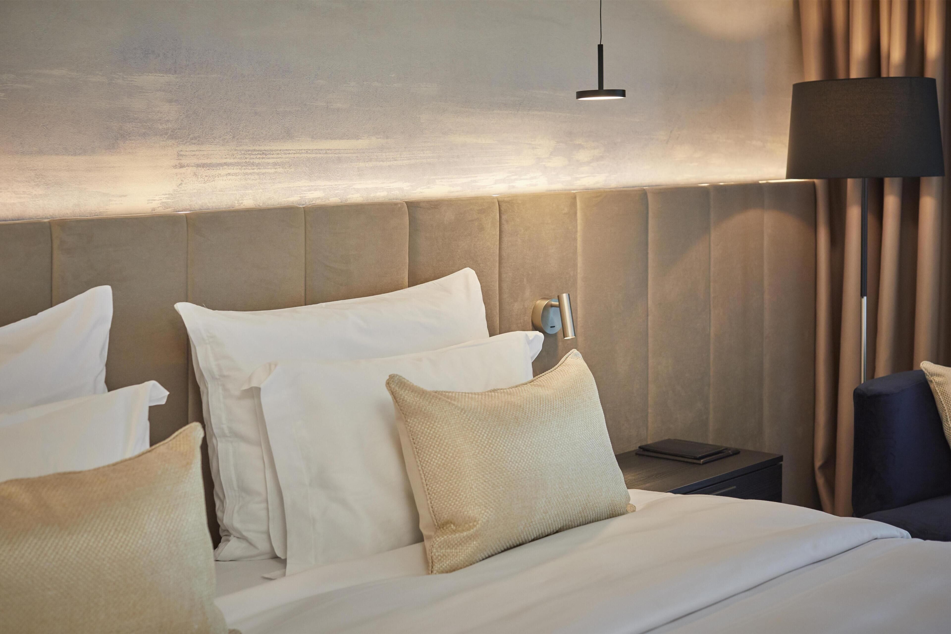 A hotel room with a large bed, a nightstand, a lamp, and a view of the outdoors.