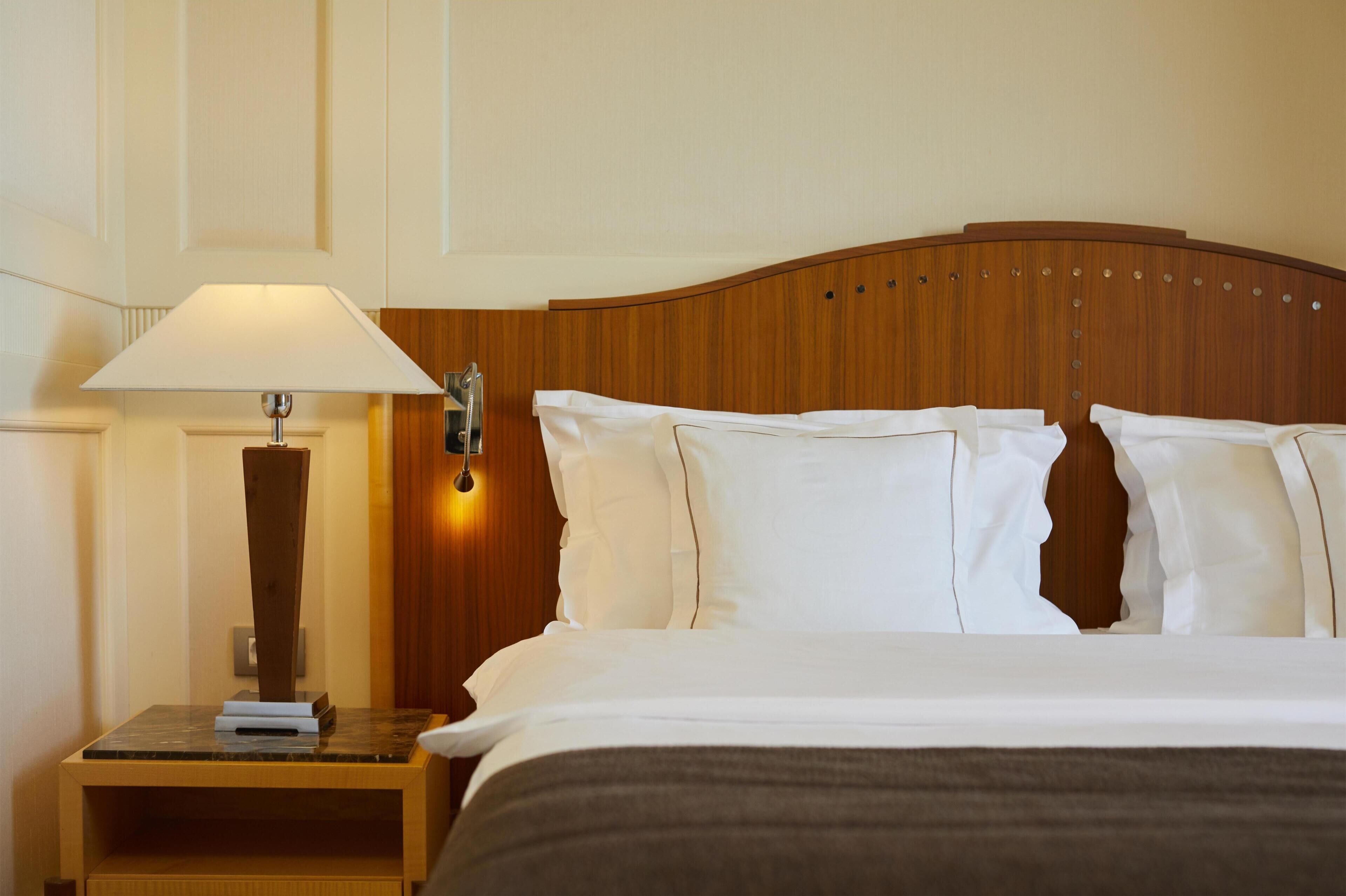 A hotel room with a bed, a nightstand with a lamp, and a wooden headboard.