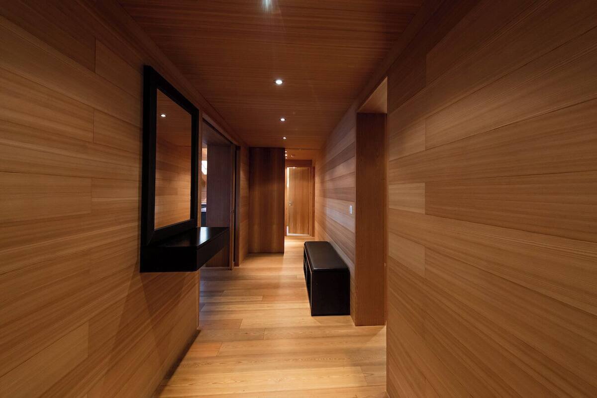 A long, narrow hallway with wooden paneling on the walls and a wooden floor. There is a bench along the right side of the hallway.