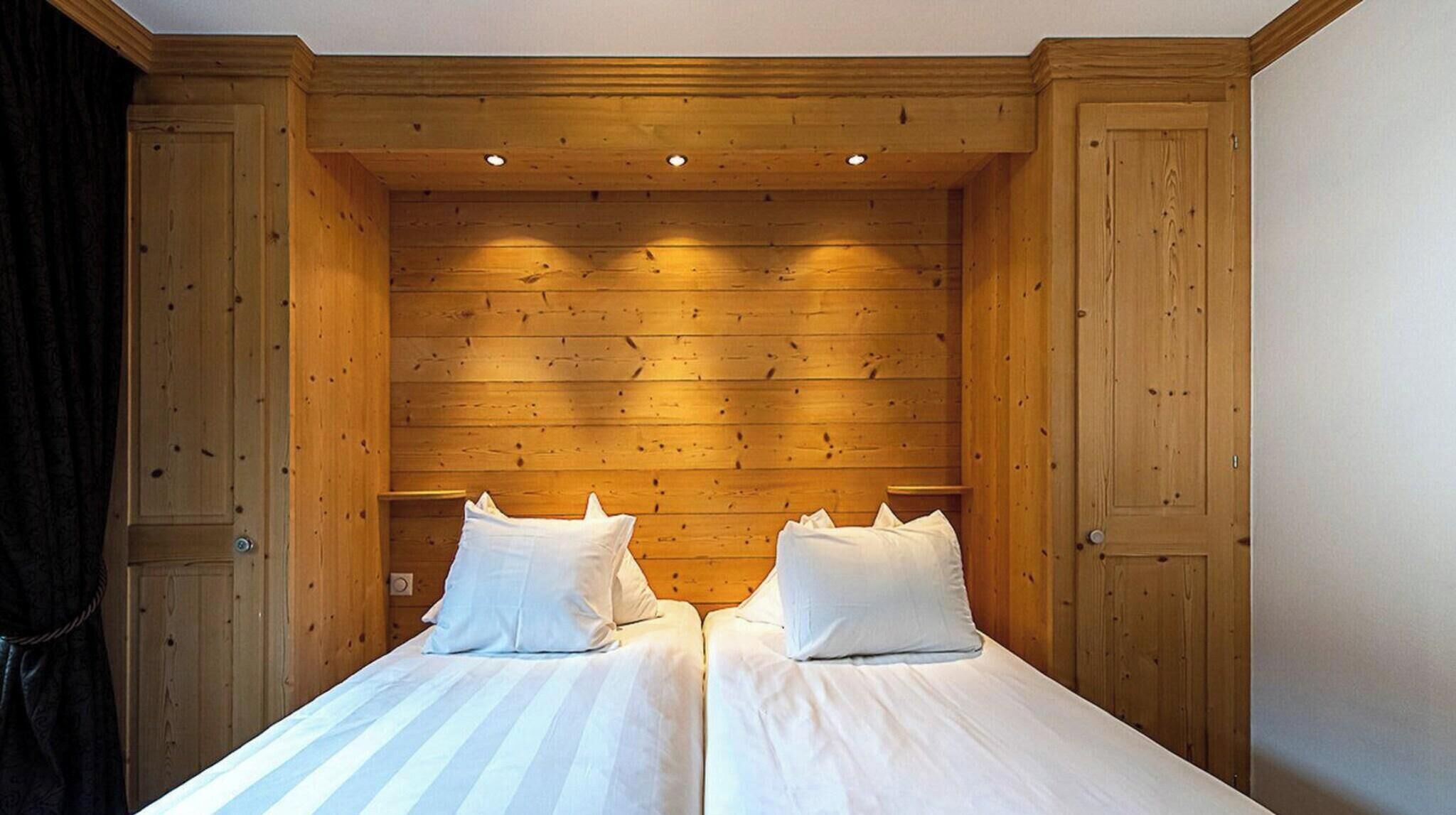 A double bed with white bedding in a wooden room with a sloped ceiling and built-in headboard.