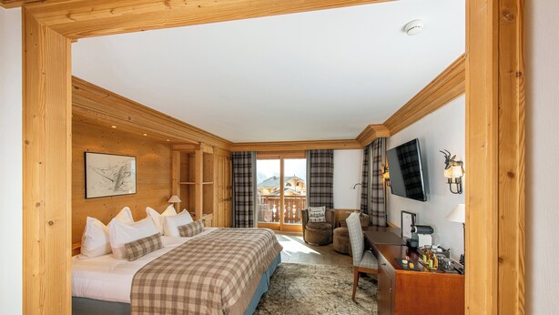 A wooden-furnished bedroom with a bed, desk, and television.