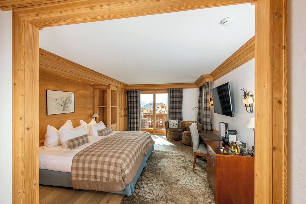 A wooden-furnished bedroom with a bed, desk, and television.