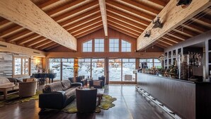 A spacious interior with a high wooden ceiling, a bar area with bottles, and a seating area with sofas and a piano.