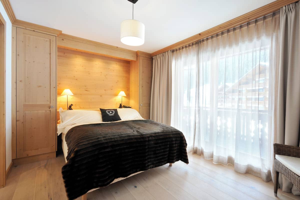 A bedroom with a bed, wooden walls, a bench, and a window with curtains.