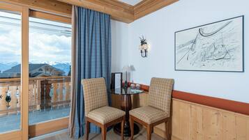 A room with a wooden ceiling, a glass door leading to a balcony, two chairs, a table with a lamp, and a framed artwork on the wall.