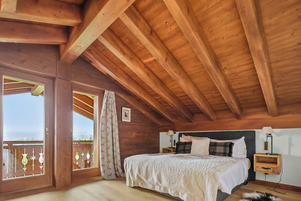 A wooden bedroom with a bed, nightstands, and a view through a large window.