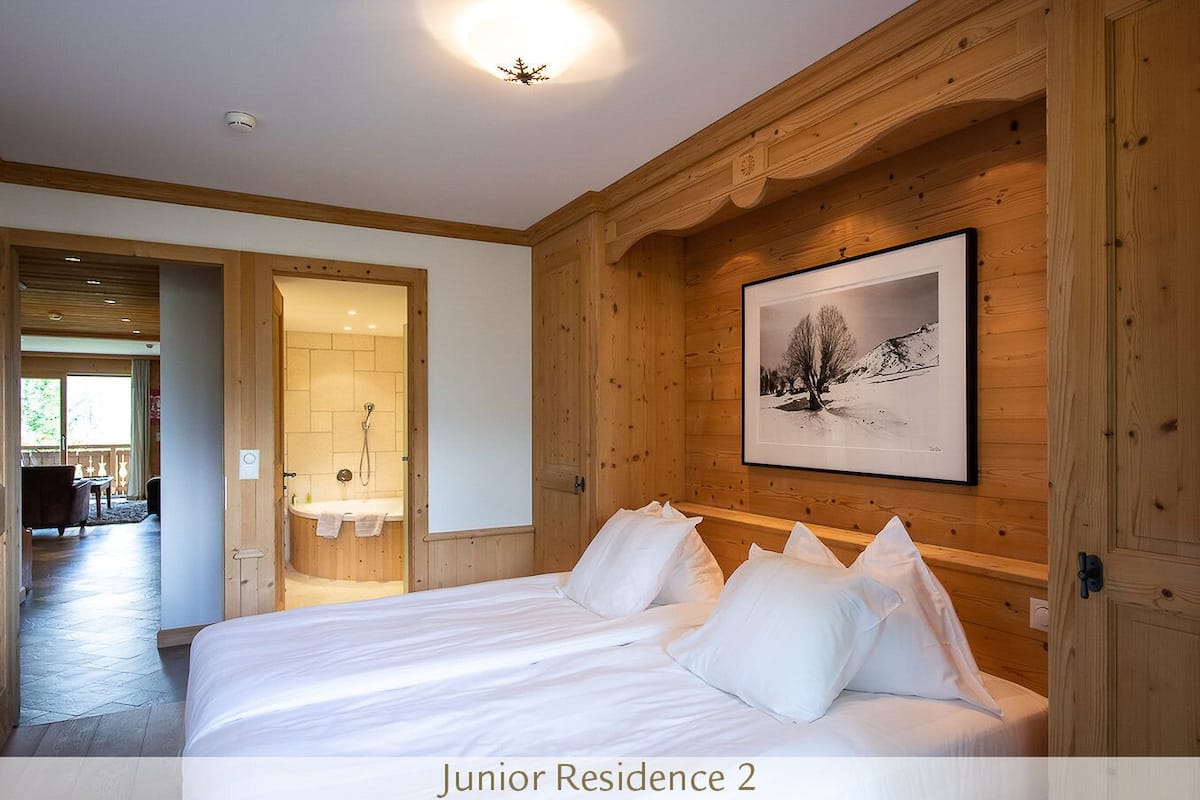 Residencia Junior de dos habitaciones con cama, paneles de madera, un cuadro enmarcado y un baño con ducha.