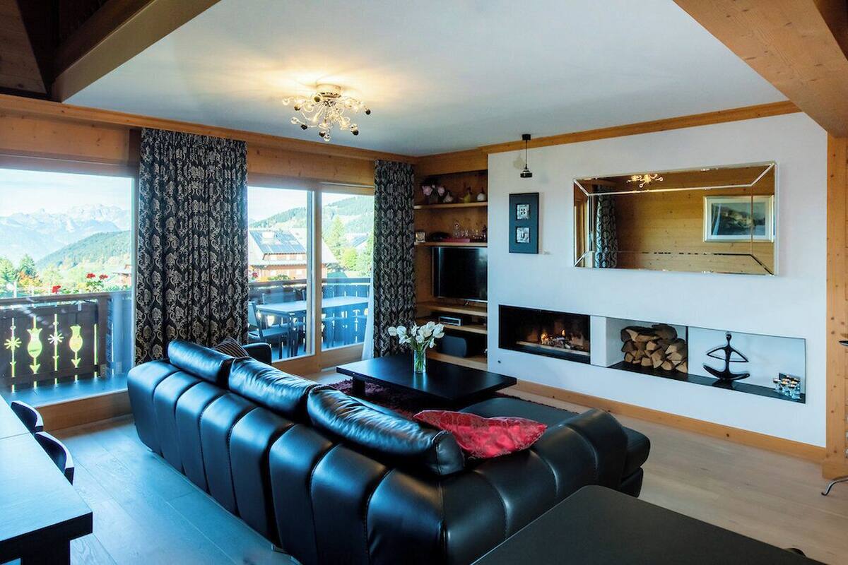 A modern living room with a black leather sofa, a dining table, and a fireplace.