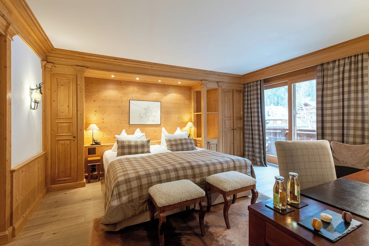 A cozy room with a large bed, wooden walls, a dining table with a view, and a fireplace.