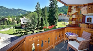 A wooden balcony with a view of a mountainous landscape, a building with a ski lift, and a restaurant area with outdoor seating. - Chalet RoyAlp Hôtel & Spa (Ollon)