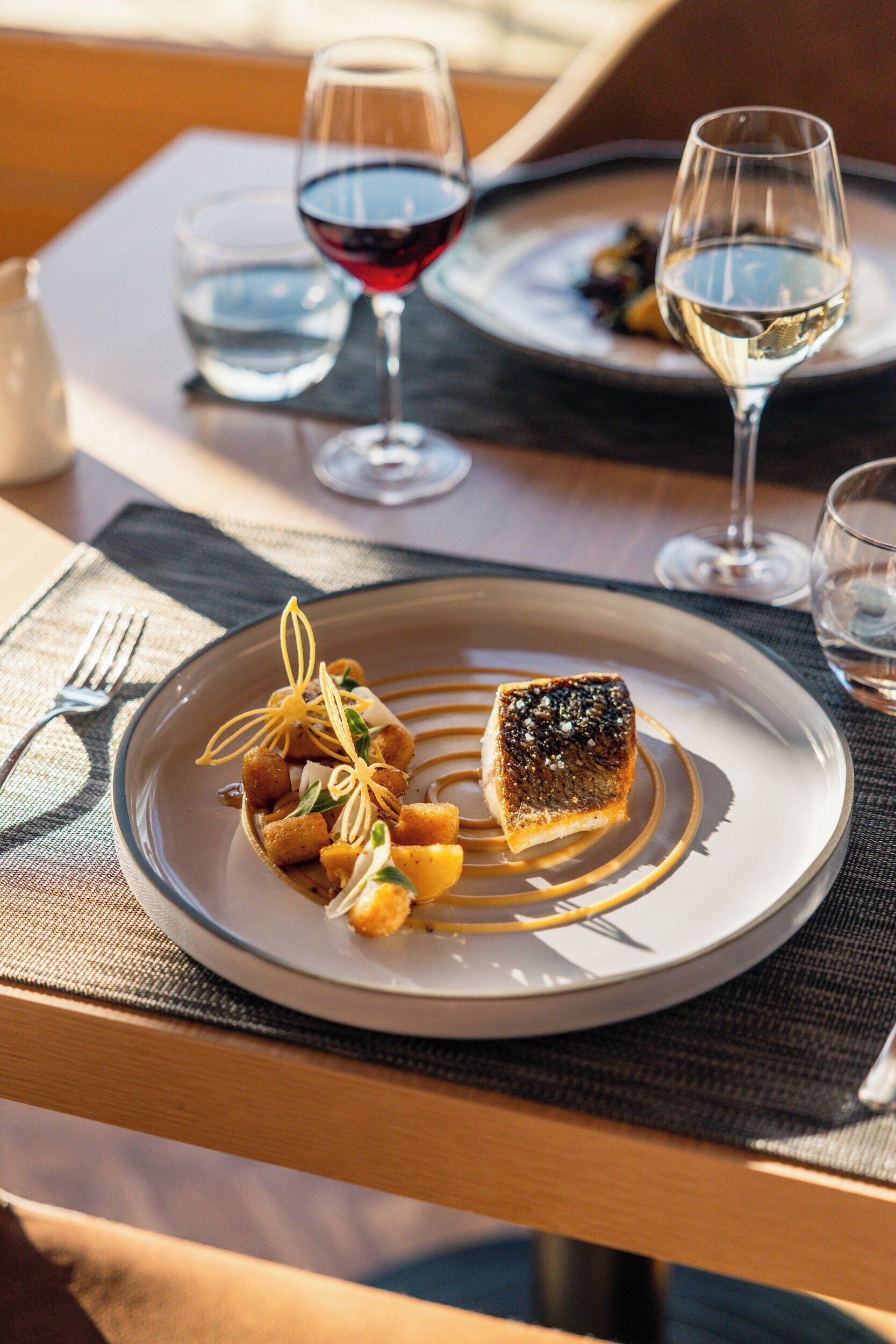 Una mesa de comedor con platos de comida, copas de vino y cubiertos.