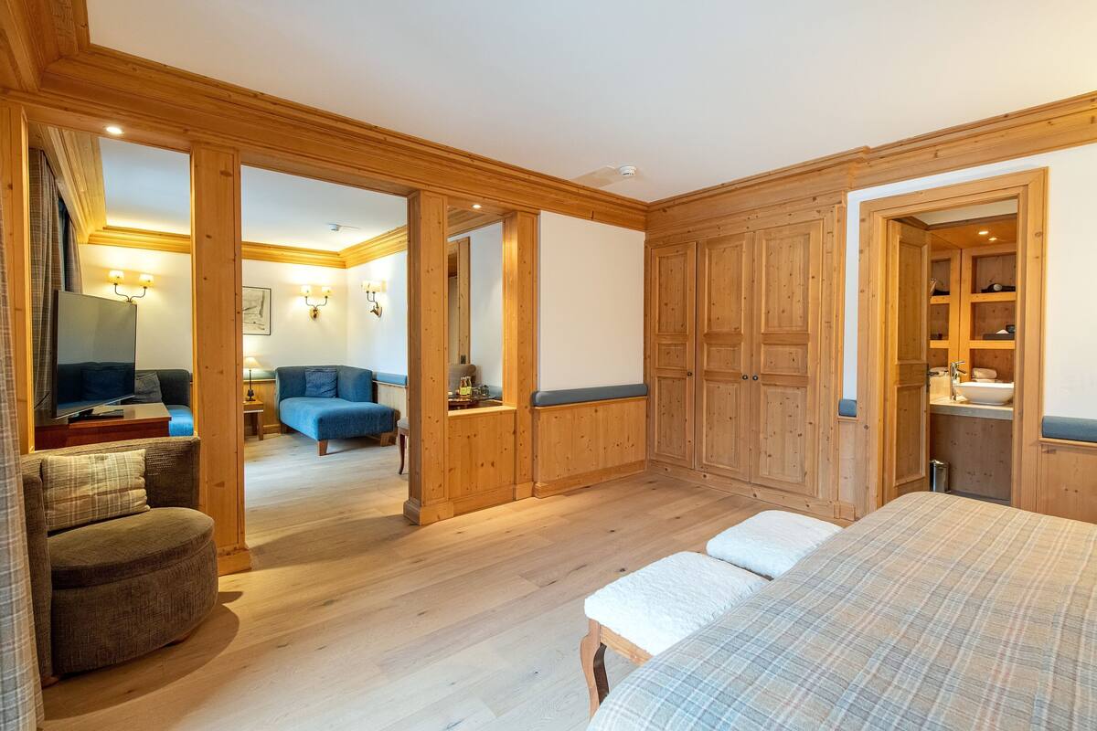 A wooden-paneled room with a bed, a sofa, a TV, and a bathroom with a sink and mirror.
