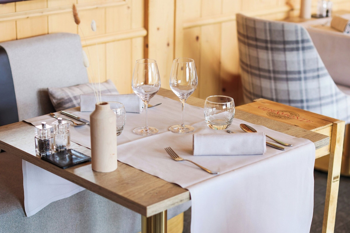 A dining table set with glasses, cutlery, and a candle, in a room with wooden walls and a sofa.
