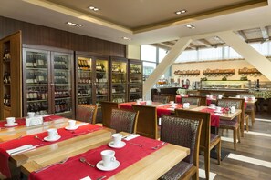 Un restaurante con varias mesas y sillas, una vitrina para vinos y una barra con una máquina de café.