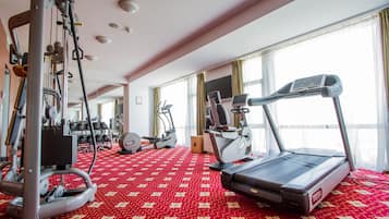 Academia de hotel com máquinas de cardio, equipamentos de peso e tapete vermelho estampado.