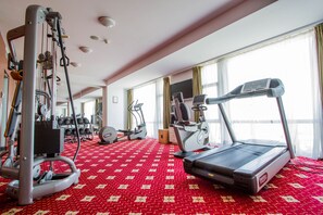 Et hotel fitnesscenter med løbebånd, styrketræningsudstyr og et rødt gulvtæppe med et mønster.