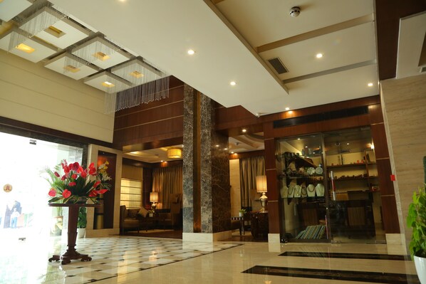 A hotel lobby with a checkered floor, a reception desk, a large potted plant, and a glass storefront displaying merchandise.
