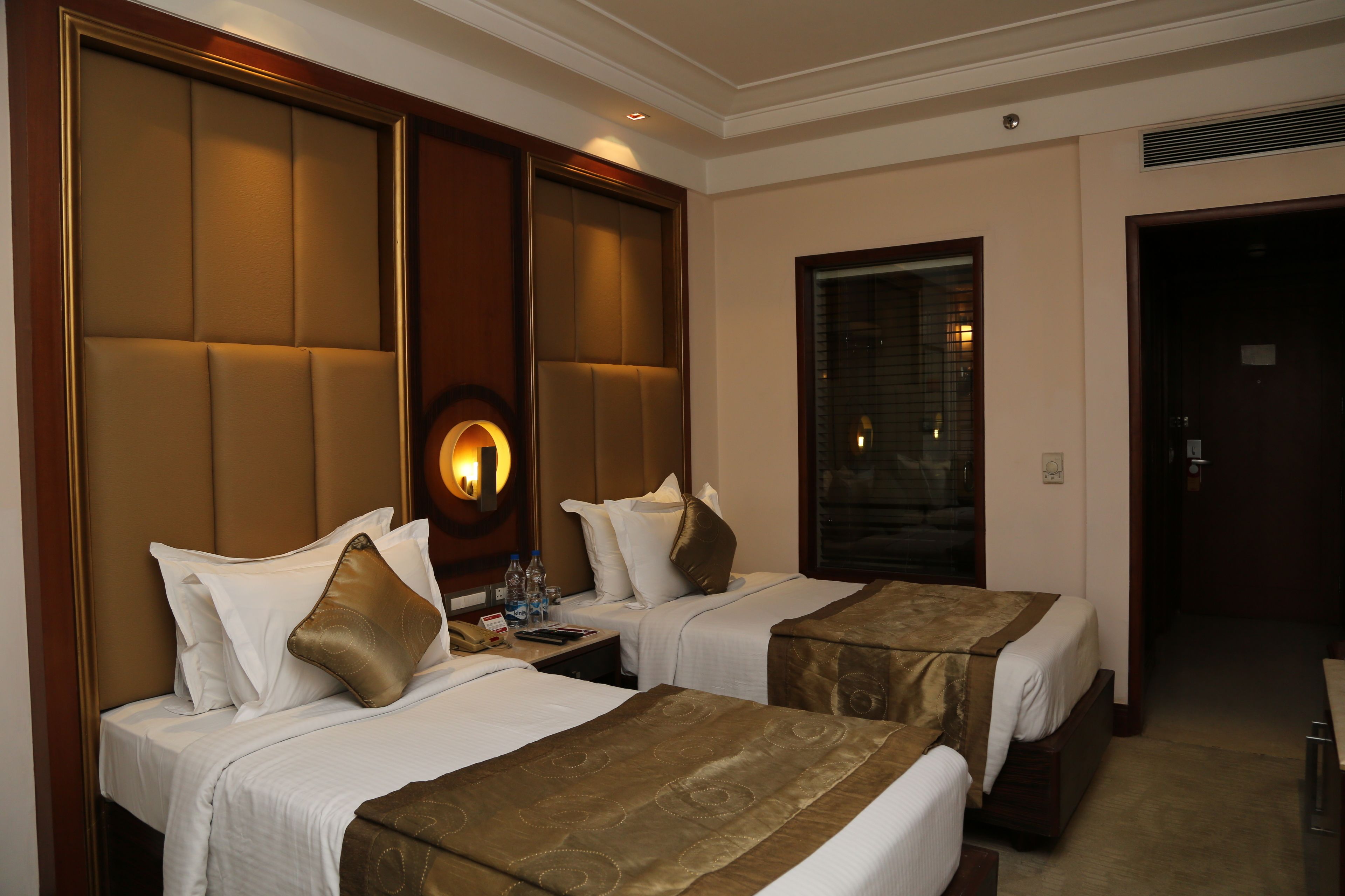Quarto de hotel com duas camas, mesa de cabeceira, abajur e um espelho grande.