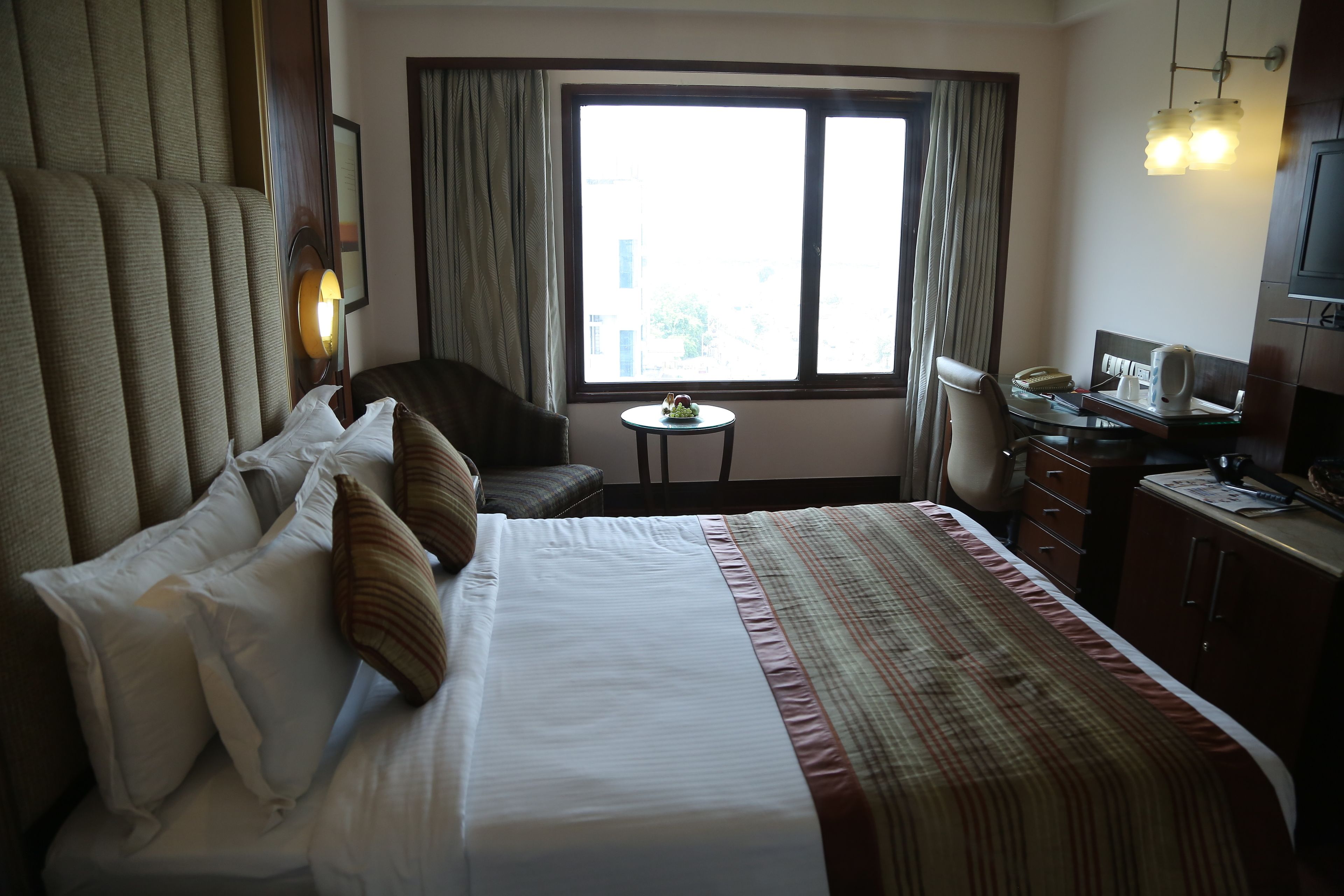 A hotel room with a bed, a desk, a chair, a small table, and a window with curtains.