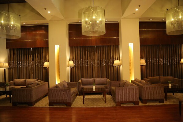 Un moderno vestíbulo de hotel con zona de estar que incluye sofás y sillones, una mesa de centro y una iluminación ambiental proveniente de candelabros.