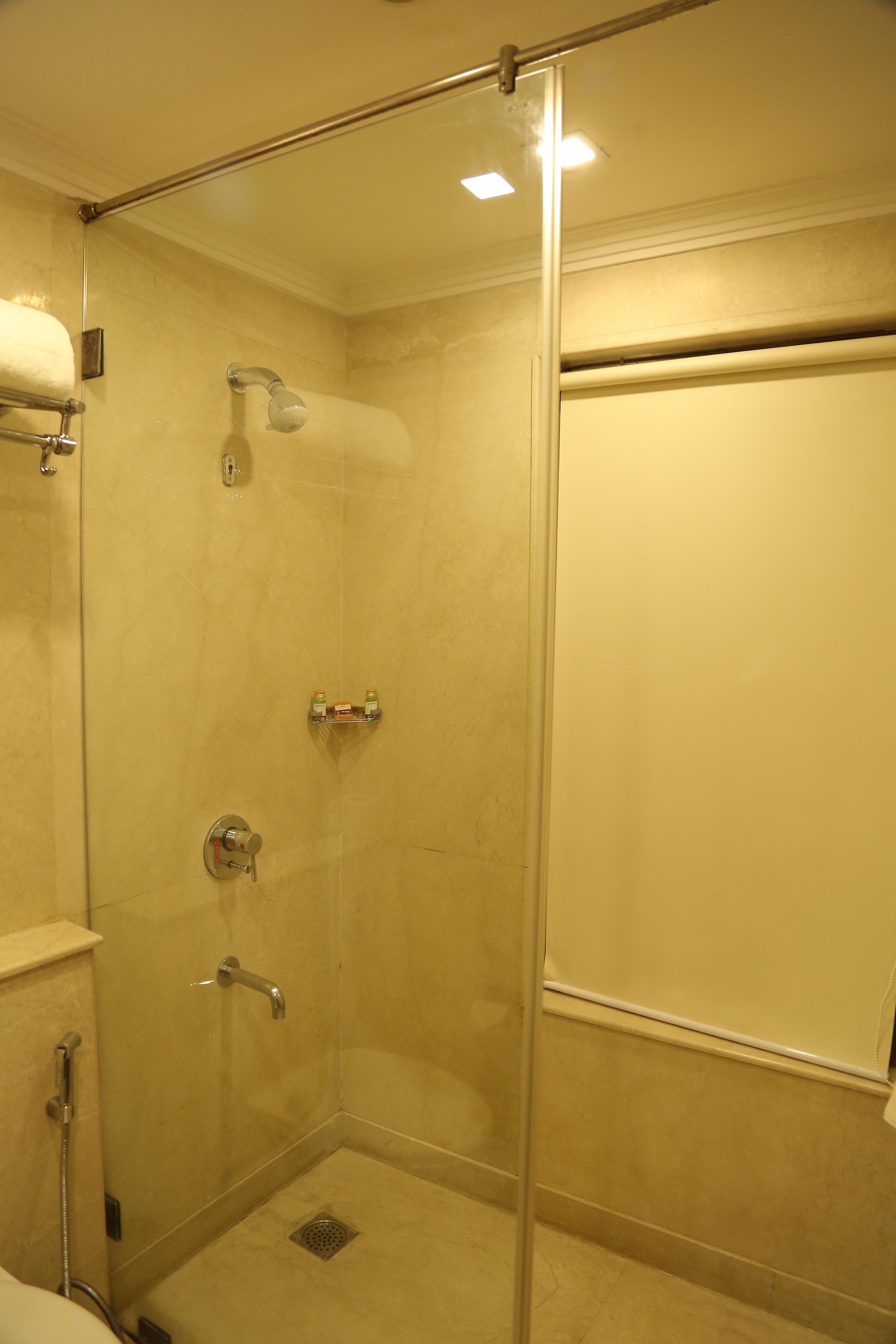 A glass-enclosed shower stall with a handheld showerhead, a handheld showerhead, and a wall-mounted faucet.