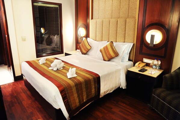Habitación de hotel con una cama grande, dos almohadas, una mesita de noche con un teléfono y una botella, y una silla.
