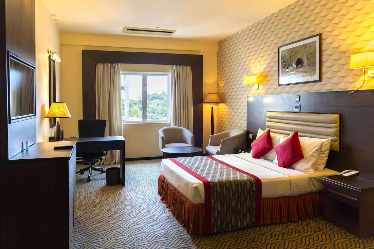 Quarto de hotel com cama, escrivaninha, cadeiras e janela com cortinas.