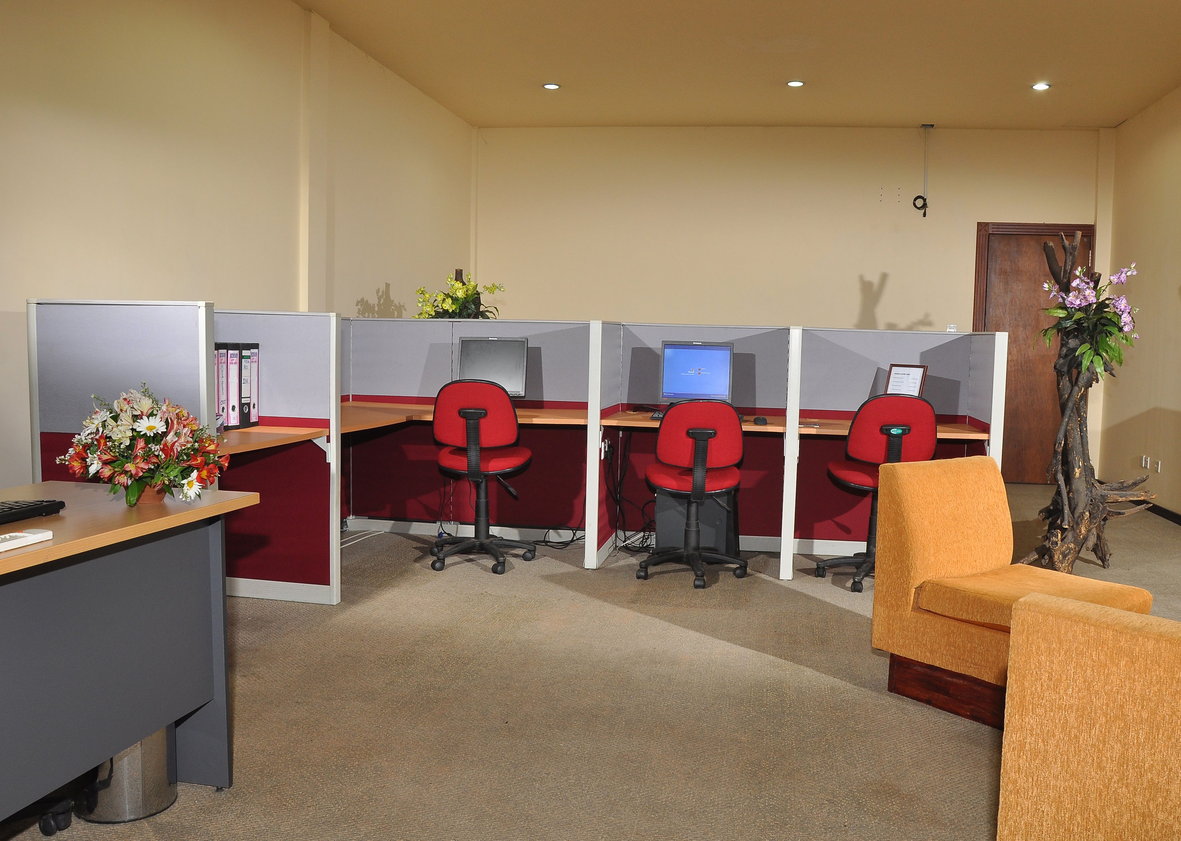 A modern office space with cubicles, red office chairs, a desk with a computer, and a plant.