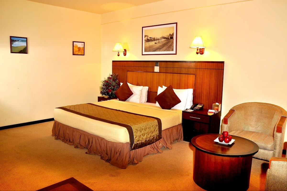 Quarto de hotel com cama, mesa de cabeceira, cadeira, mesa redonda e abajur.