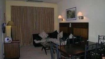 Una habitación con una mesa de comedor, sillas, un sofá, una lámpara y un cuadro en la pared.