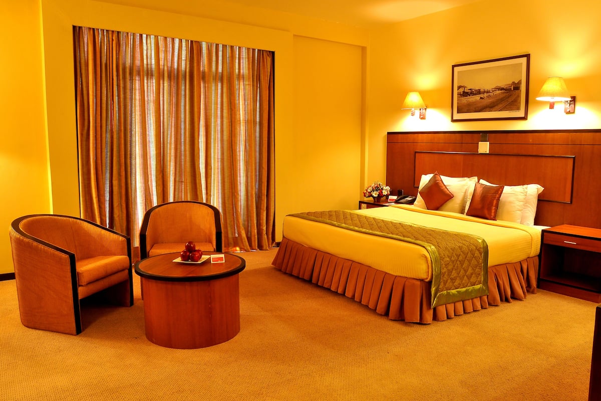 Quarto de hotel com uma cama grande, duas poltronas, uma mesa redonda pequena e uma mesa de cabeceira.