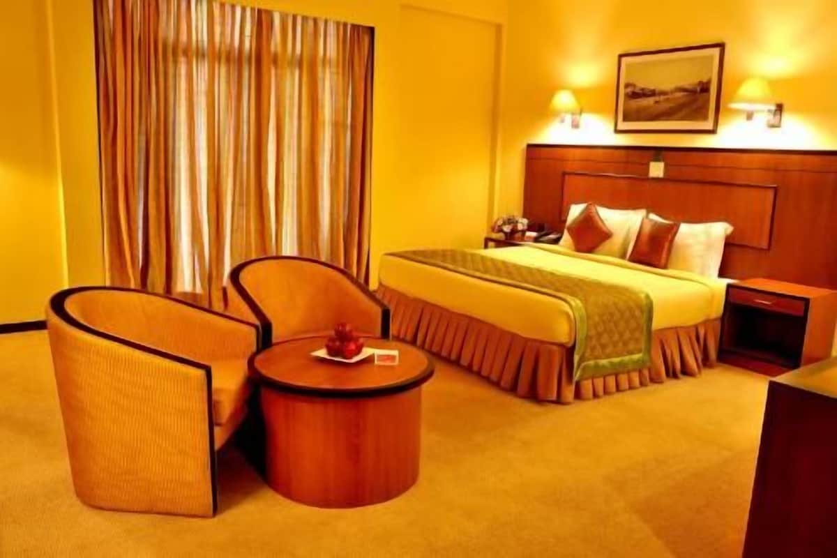 Una habitación de hotel con una cama, dos sillones, una mesita y una mesita de noche.