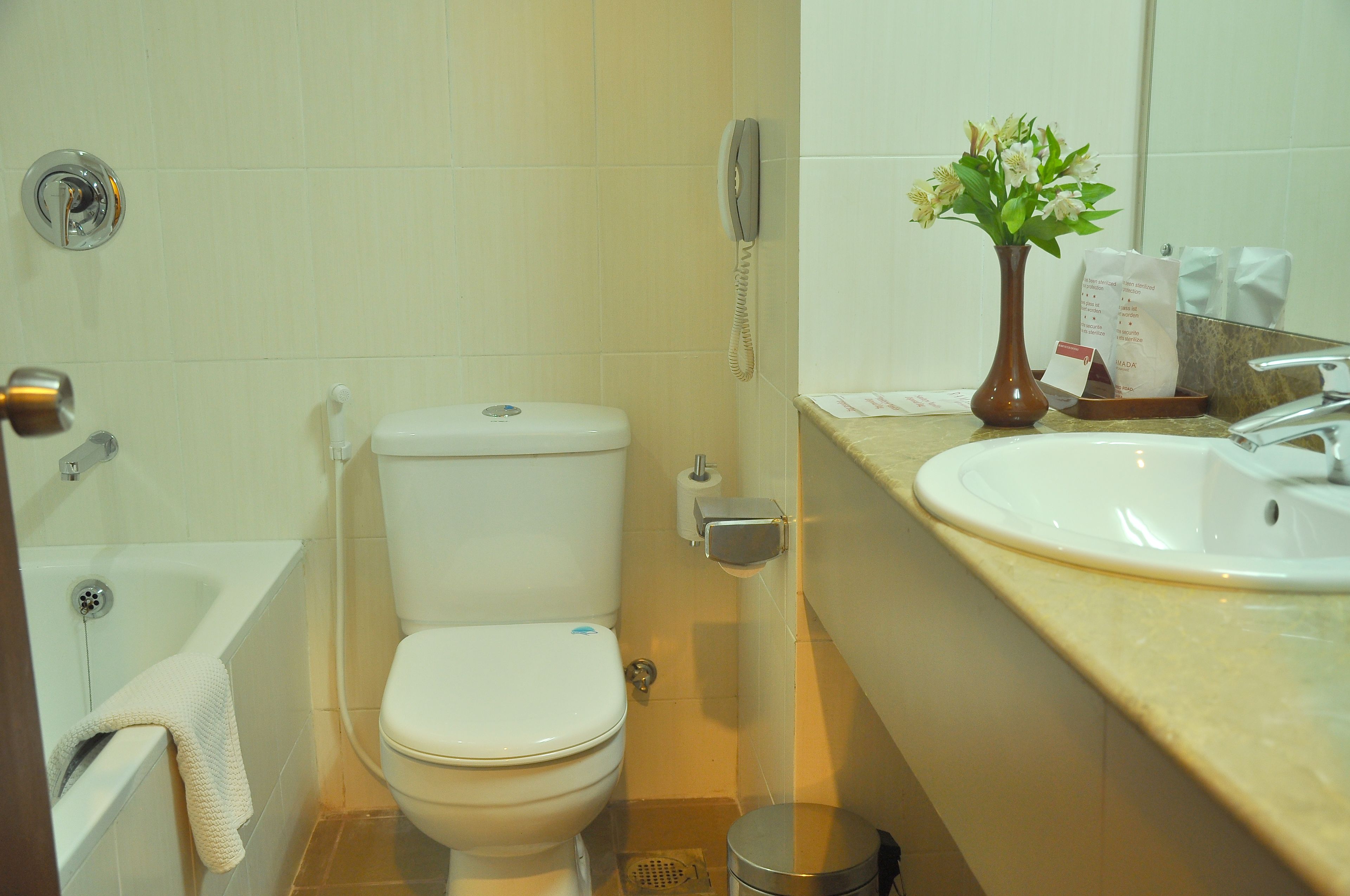A bathroom with a toilet, a sink, a telephone, and a trash can.