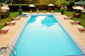 Ein rechteckiger Pool mit Fliesenrand, umgeben von Liegestühlen und Sonnenschirmen.