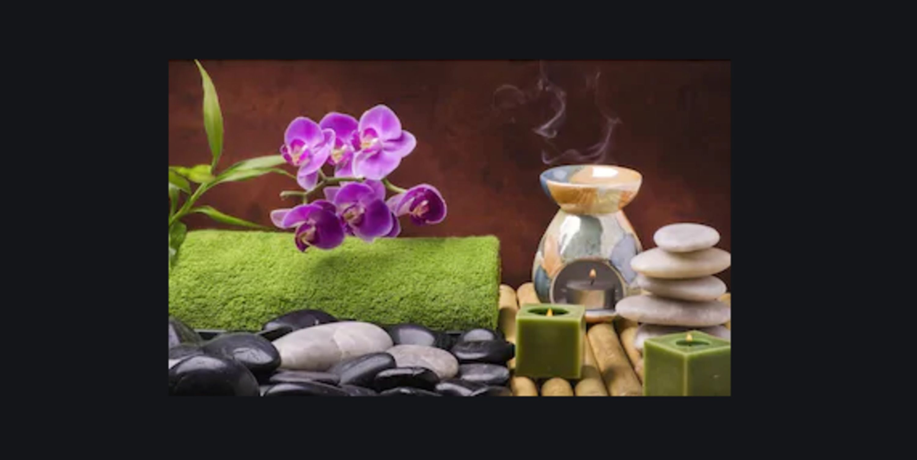 A spa setting with a purple orchid, green moss, black and white stones, and a stack of stones.