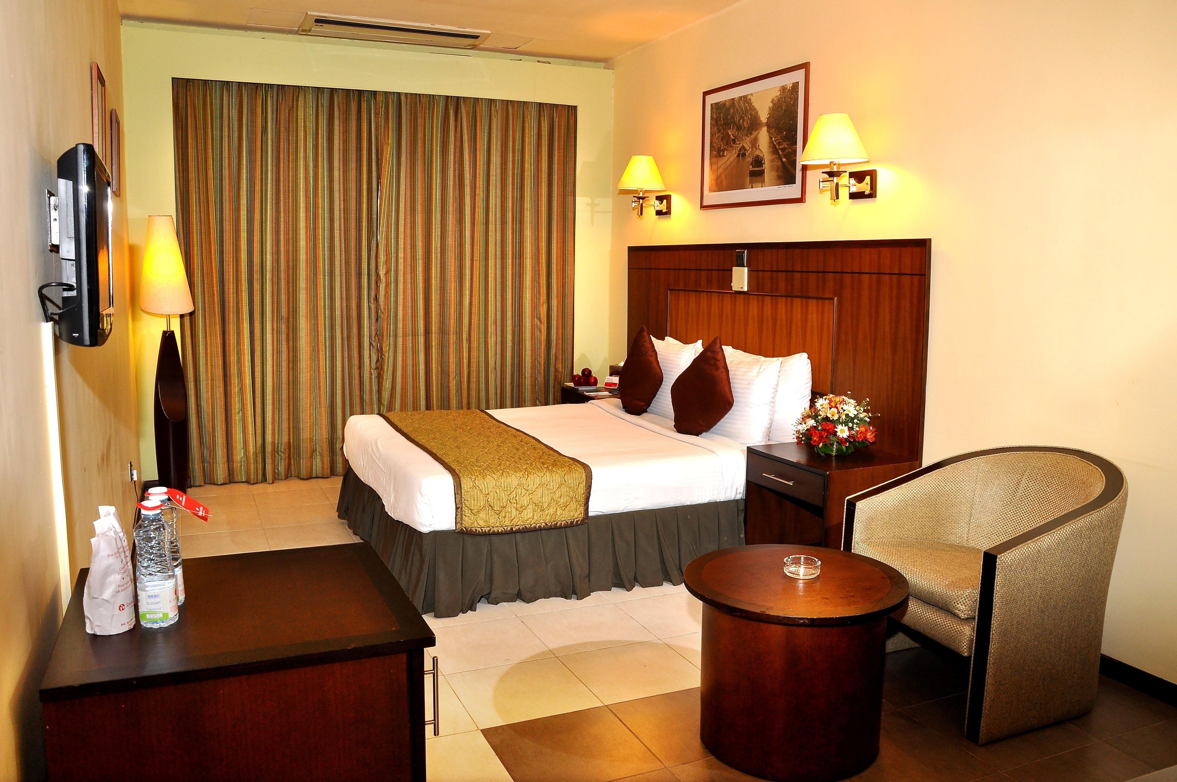 A hotel room with a bed, bedside table, chair, and a television.