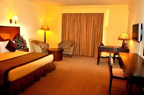 Ein Hotelzimmer mit einem großen Bett, zwei Sesseln, einem kleinen Tisch, einem Schreibtisch und einem Fernseher.