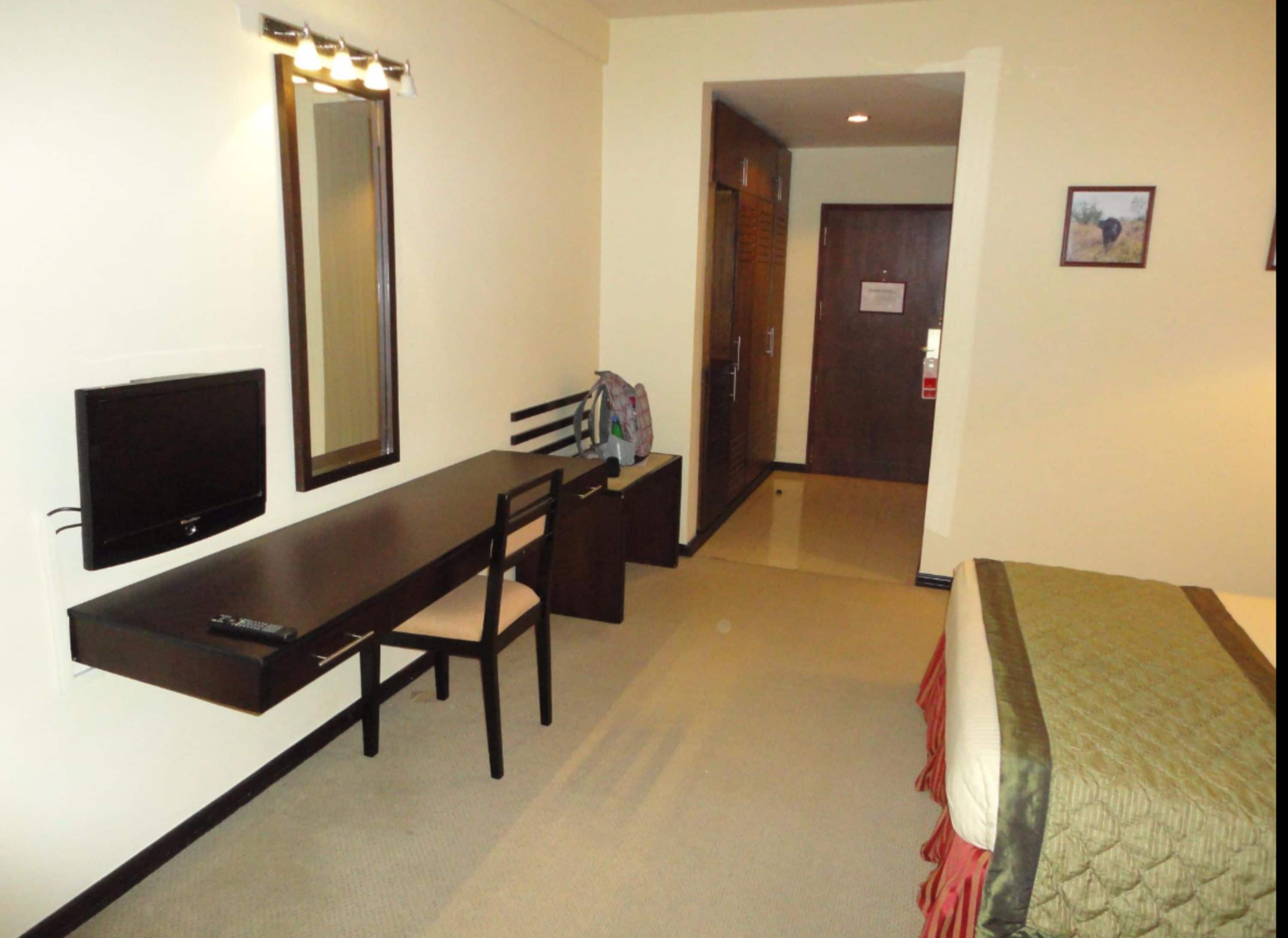 A hotel room with a bed, a desk with a chair, a television, and a mirror.