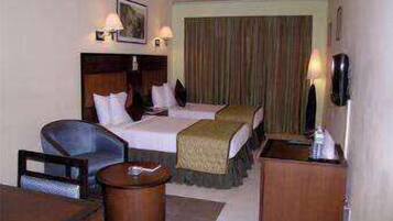 A hotel room with two beds, a desk, a chair, a small table, and a bedside table.