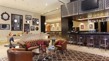 A hotel lobby with a bar area, leather seating, and artwork on the walls.