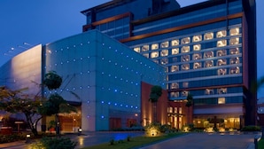 Un hotel moderno con fachada de vidrio, varios pisos y una entrada bien iluminada.