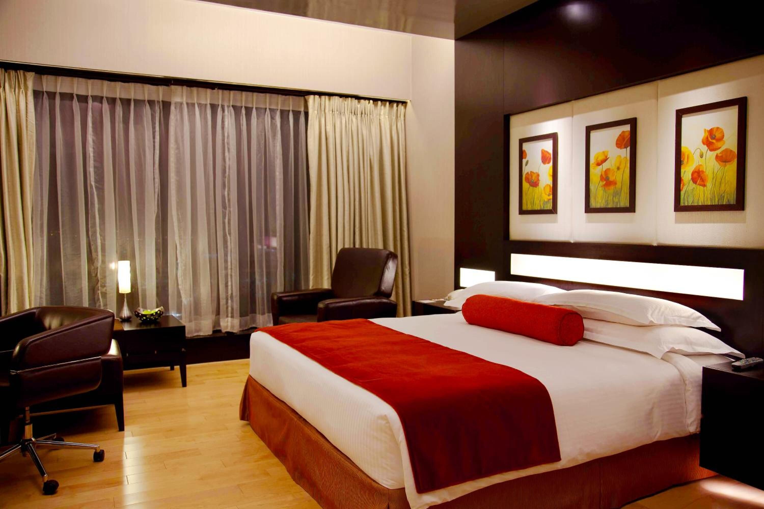 Una habitación de hotel con una cama grande, un escritorio, una silla y un ventanal con cortinas.