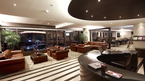 Un amplio y moderno salón con sofás de cuero, un mostrador de recepción y ventanas grandes con vistas a la ciudad.