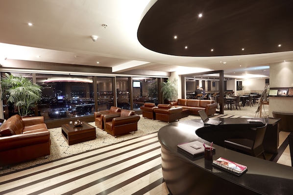 A spacious, modern lounge area with leather sofas, a reception desk, and large windows offering a city view. - The Oterra Bengaluru Electronics City (Bengaluru)
