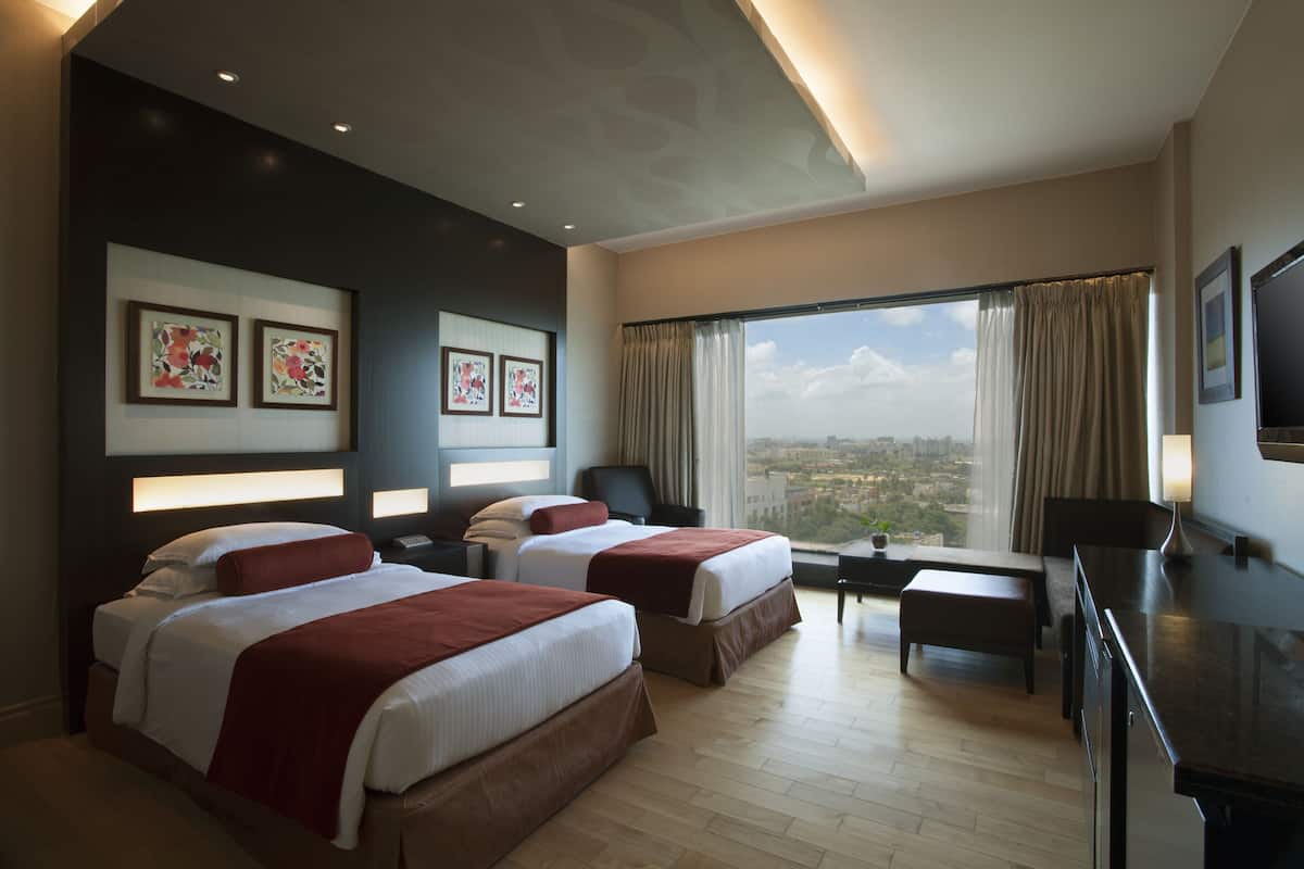 A hotel room with two beds, a desk, a chair, and a TV.