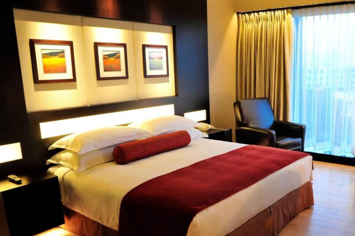 A hotel room with a large bed, a nightstand, a chair, and a window with curtains.