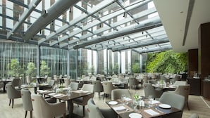 Un restaurante espacioso con techos altos y ventanas amplias, con mobiliario moderno y una pared verde.