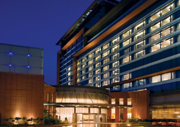 Un hotel moderno con fachada de vidrio, varios pisos y una entrada bien iluminada.