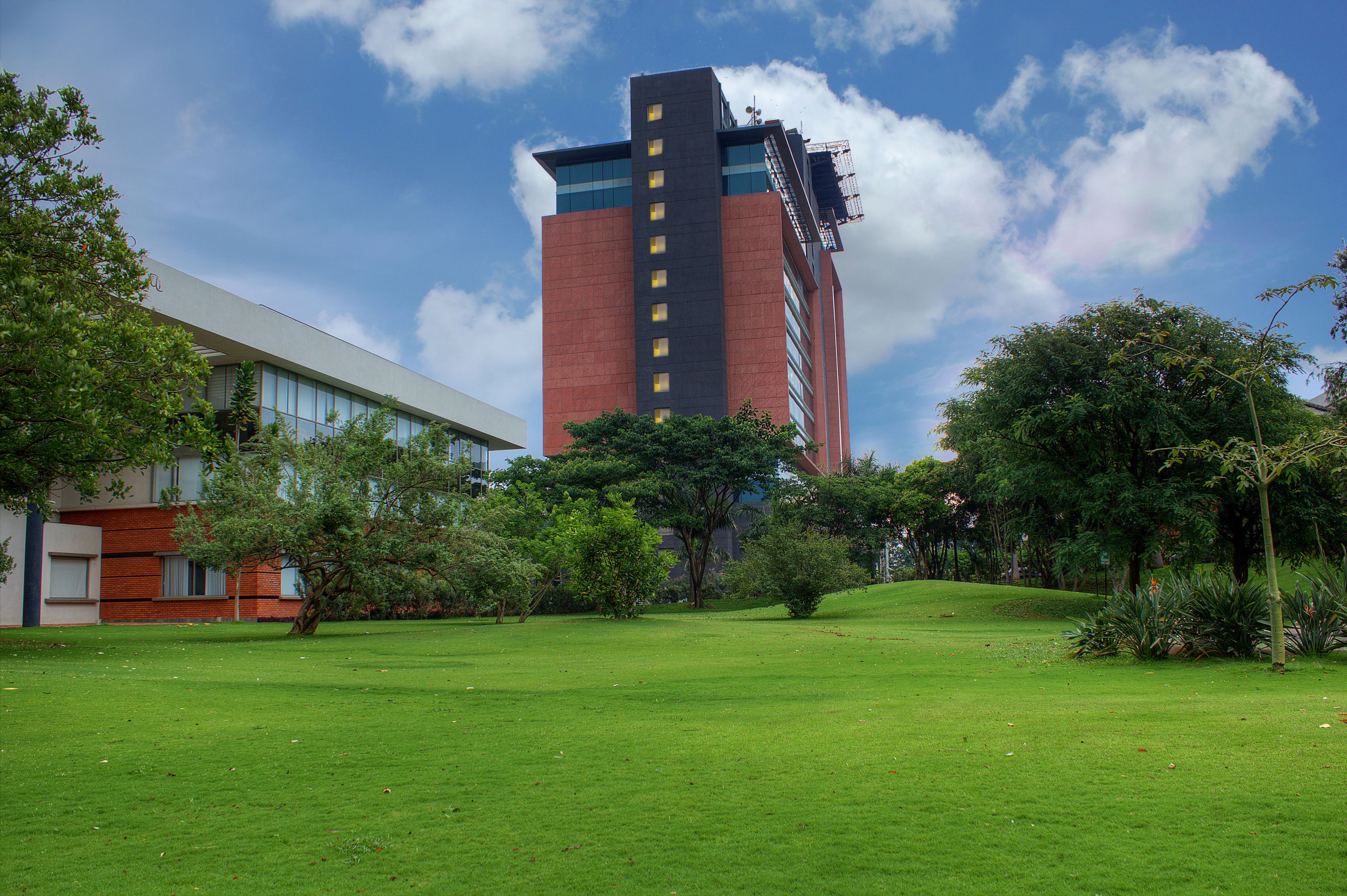A modern building with a red facade and a glass section, surrounded by a well-maintained grassy area with trees and shrubs.