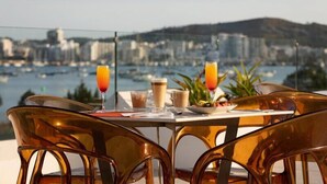 A table with breakfast items and drinks, overlooking a marina and cityscape. - Hotel THB Naeco Ibiza - Adults Only (Sant Josep de sa Talaia)